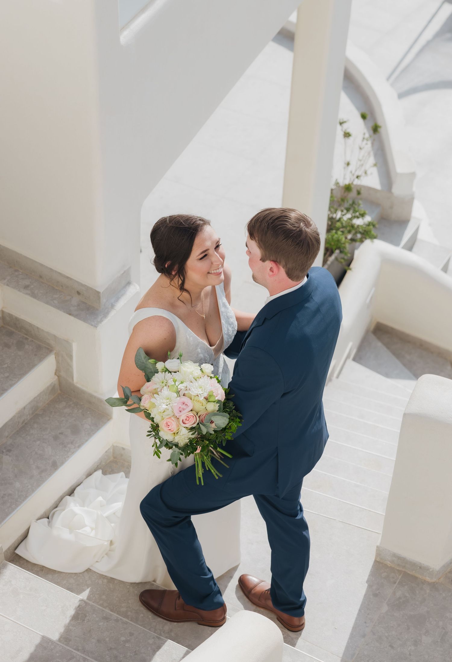 Bride and groom embracing on white stone staircase at Santorini destination wedding