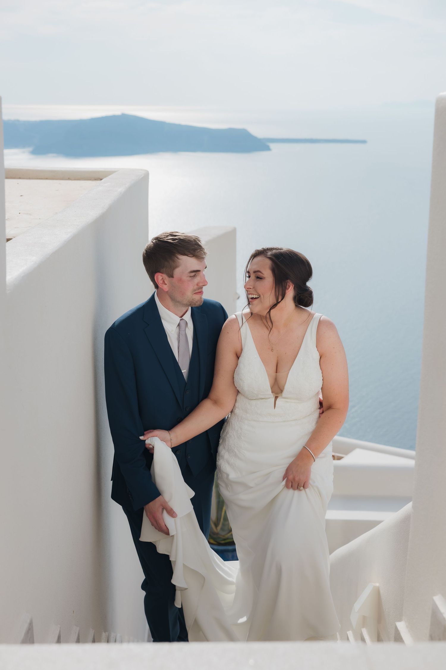 Newlyweds smiling against white wall with ocean view during Santorini cliffside wedding