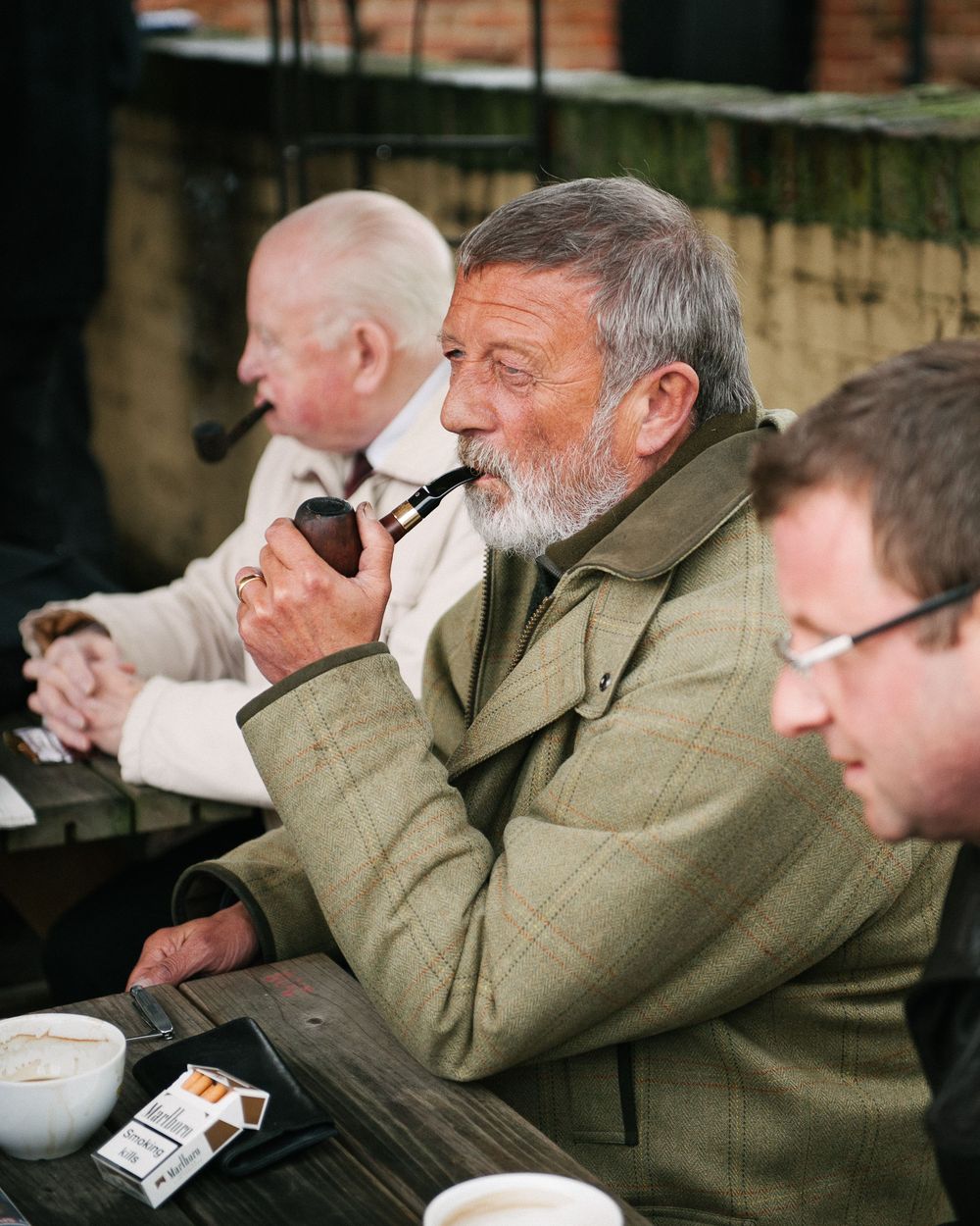 Group of pipe smokers gathered outdoors in casual conversation.