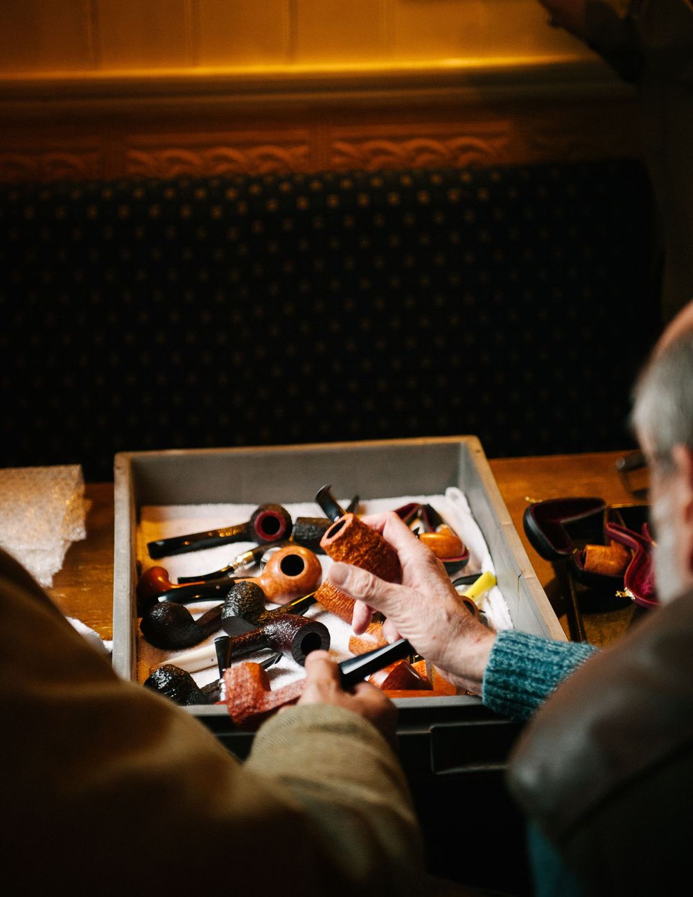 Collection of vintage pipes displayed in wooden cases under warm lighting.