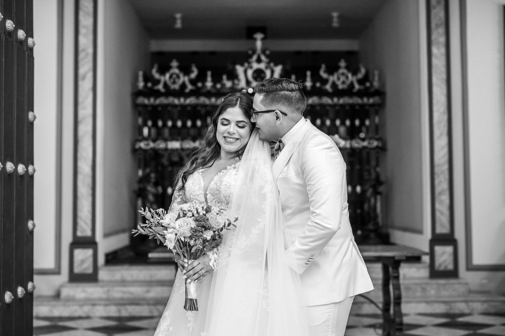 Black and white photo shows two people in traditional wedding attire standing together in an elegant venue.