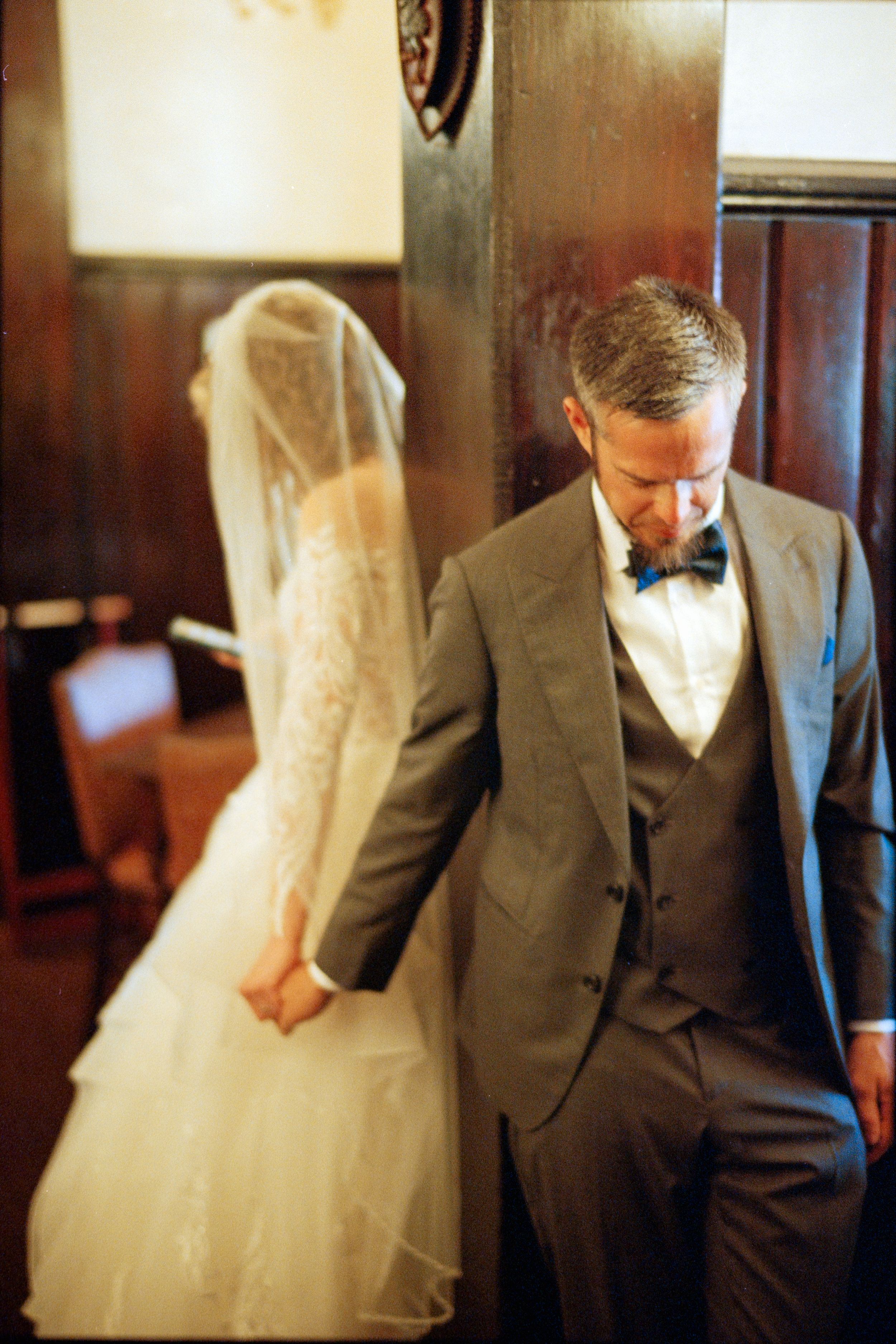 A couple shares an intimate moment before their wedding ceremony, with the bride in a white veil and groom in a gray suit.
