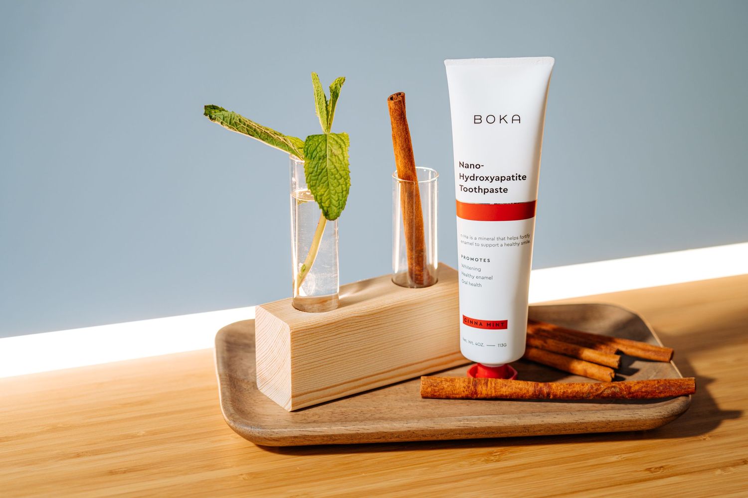 Skincare products and electric toothbrush arranged on wooden tray with mint garnish.