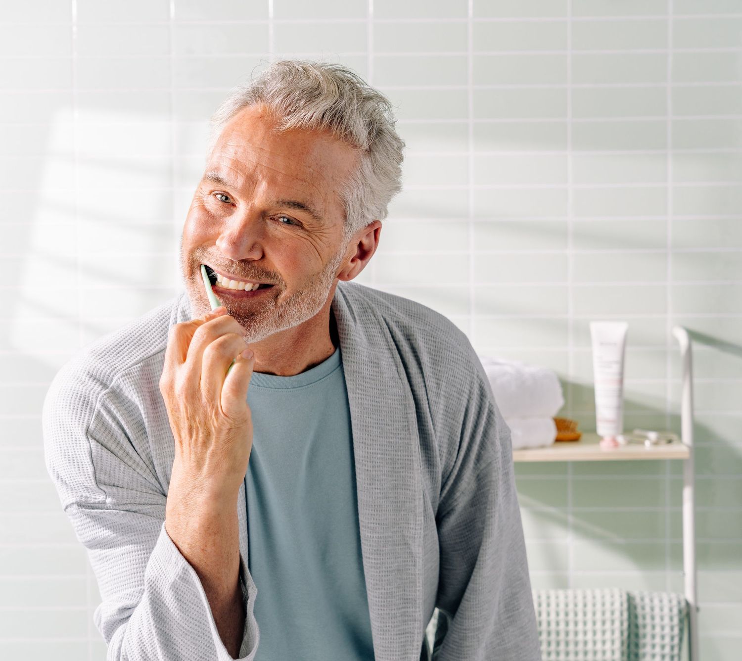 Smiling mature person in grey cardigan and blue shirt against bright interior background.
