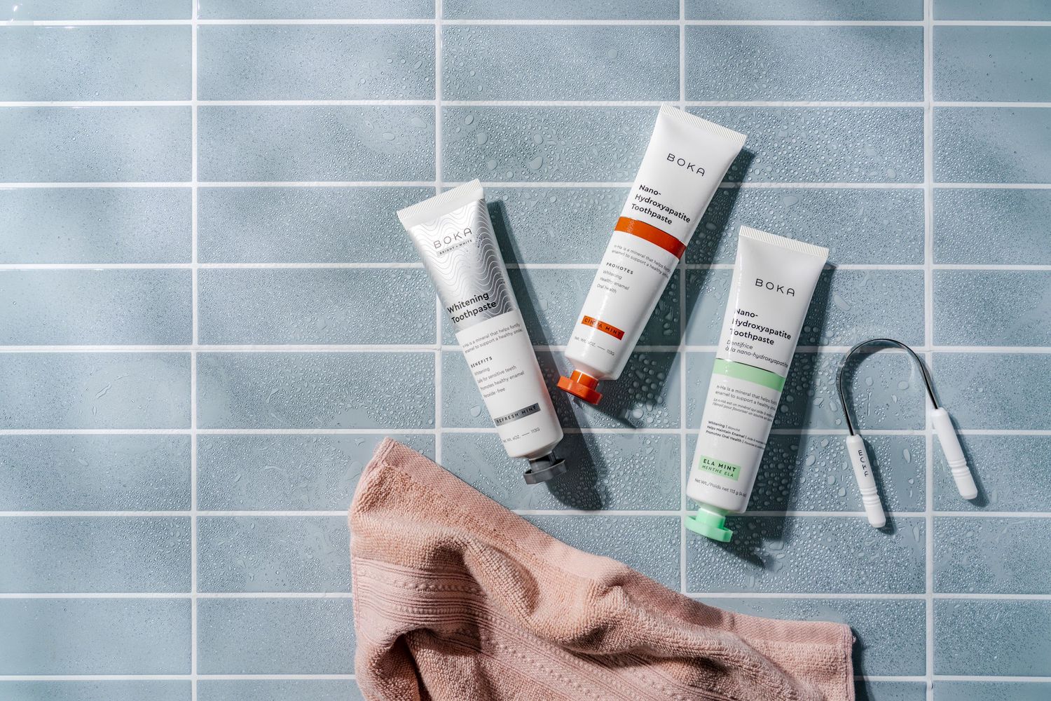 Collection of skincare tubes arranged with brown towel against blue tiled background.