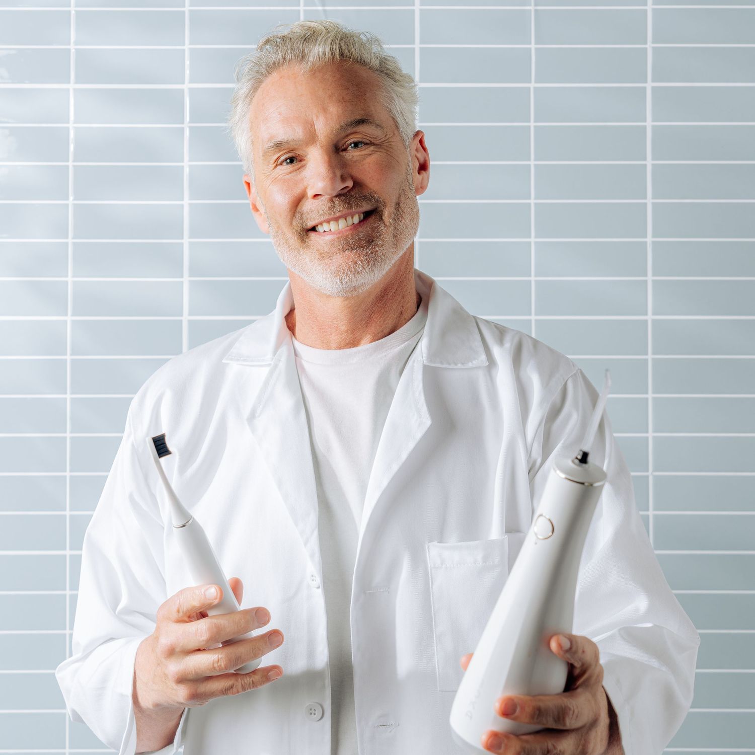 Healthcare professional in white coat holding skincare products against tiled wall.