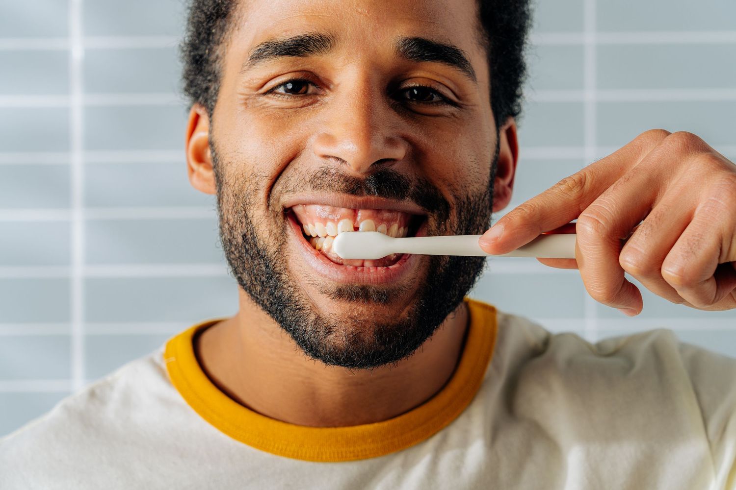 Person brushing teeth with eco-friendly toothbrush against tiled bathroom wall.