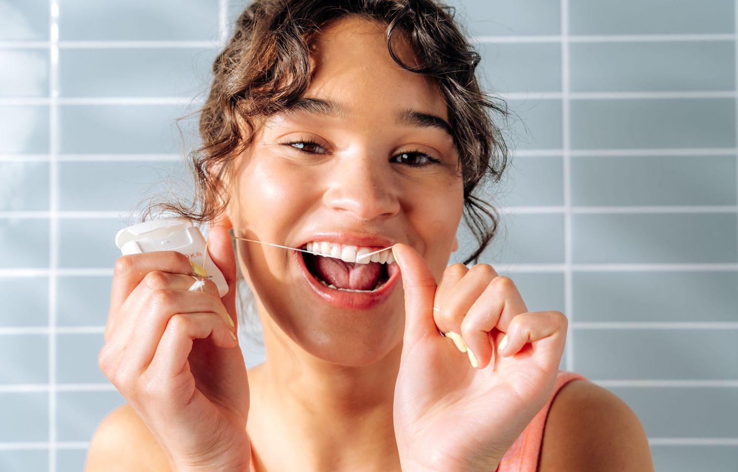 Person showing excitement while holding dental floss against blue tiled background.