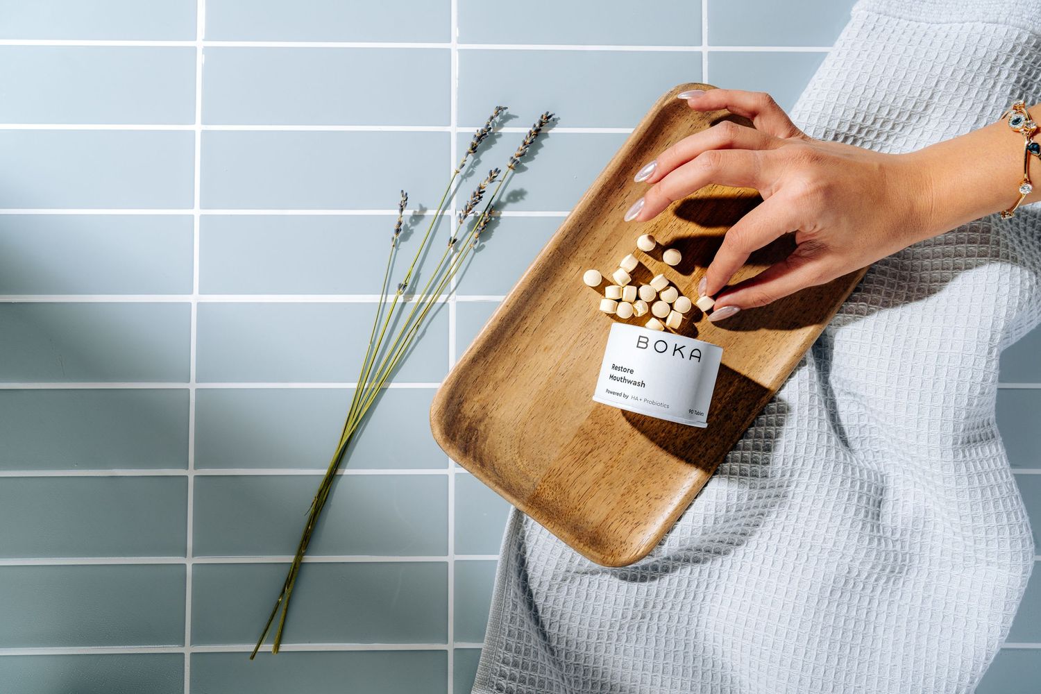 Hands arranging skincare products on wooden tray with lavender sprigs.