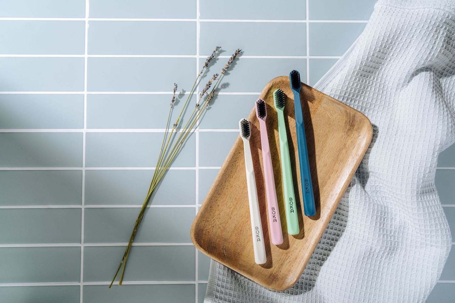Bamboo toothbrushes arranged on wooden tray with lavender sprigs and white fabric.