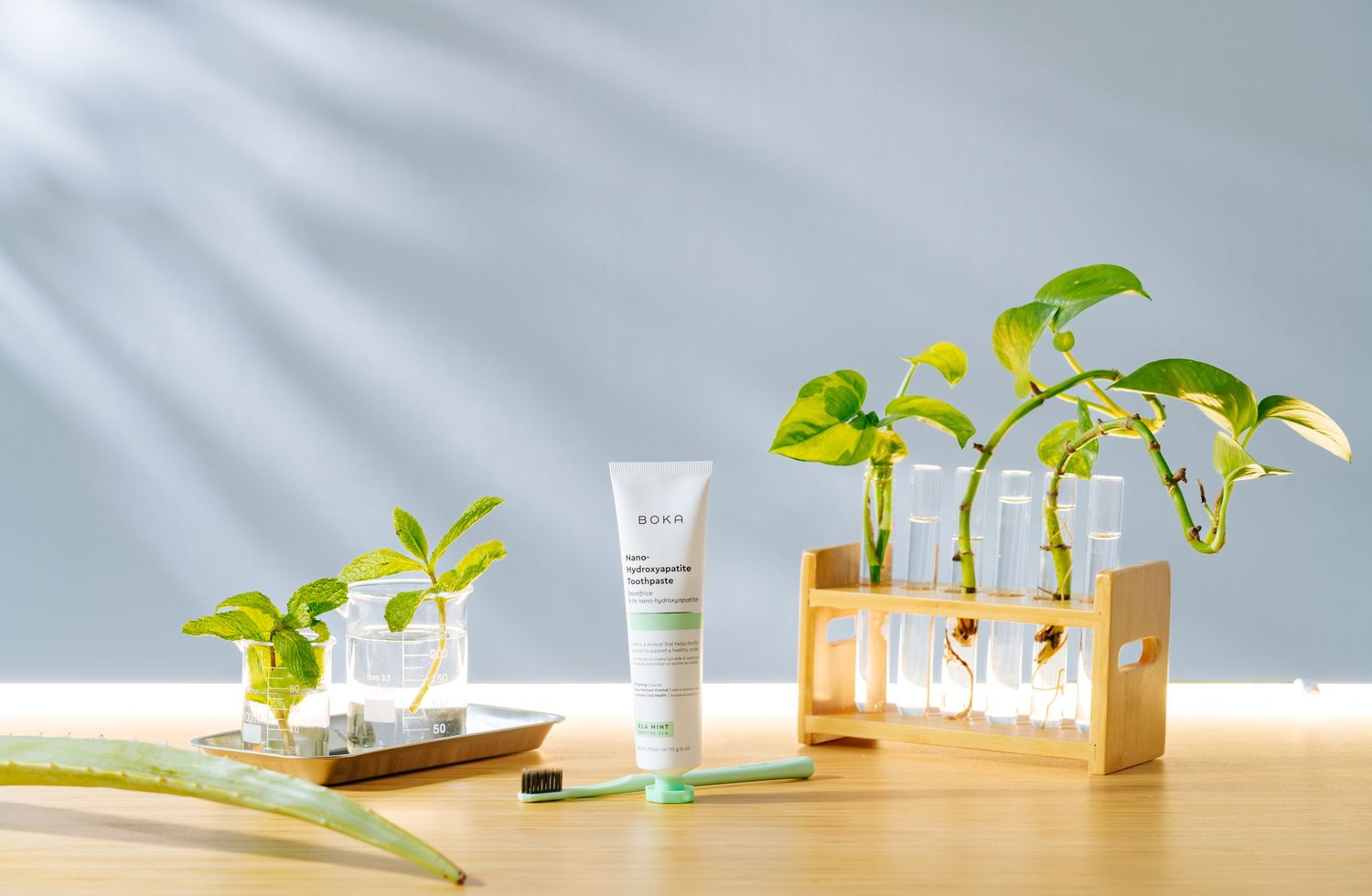 Small green plants growing in glass containers with skincare product on wooden surface.