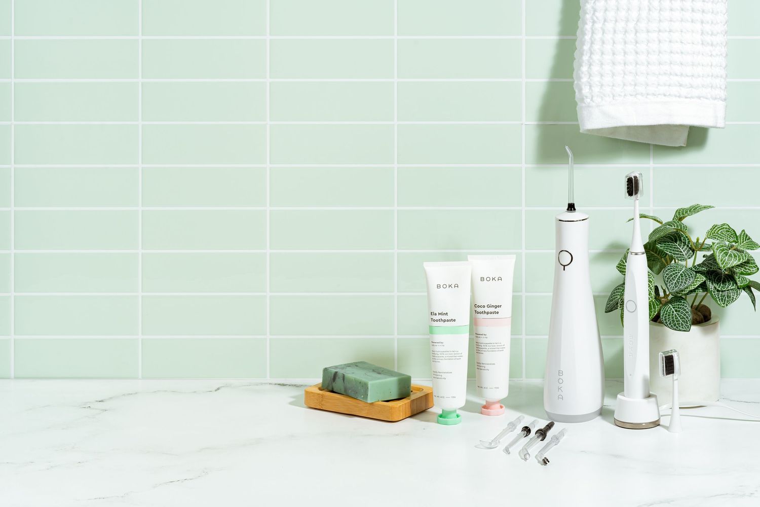 Minimalist bathroom setup with skincare products, electric toothbrush and green plants against mint wall.