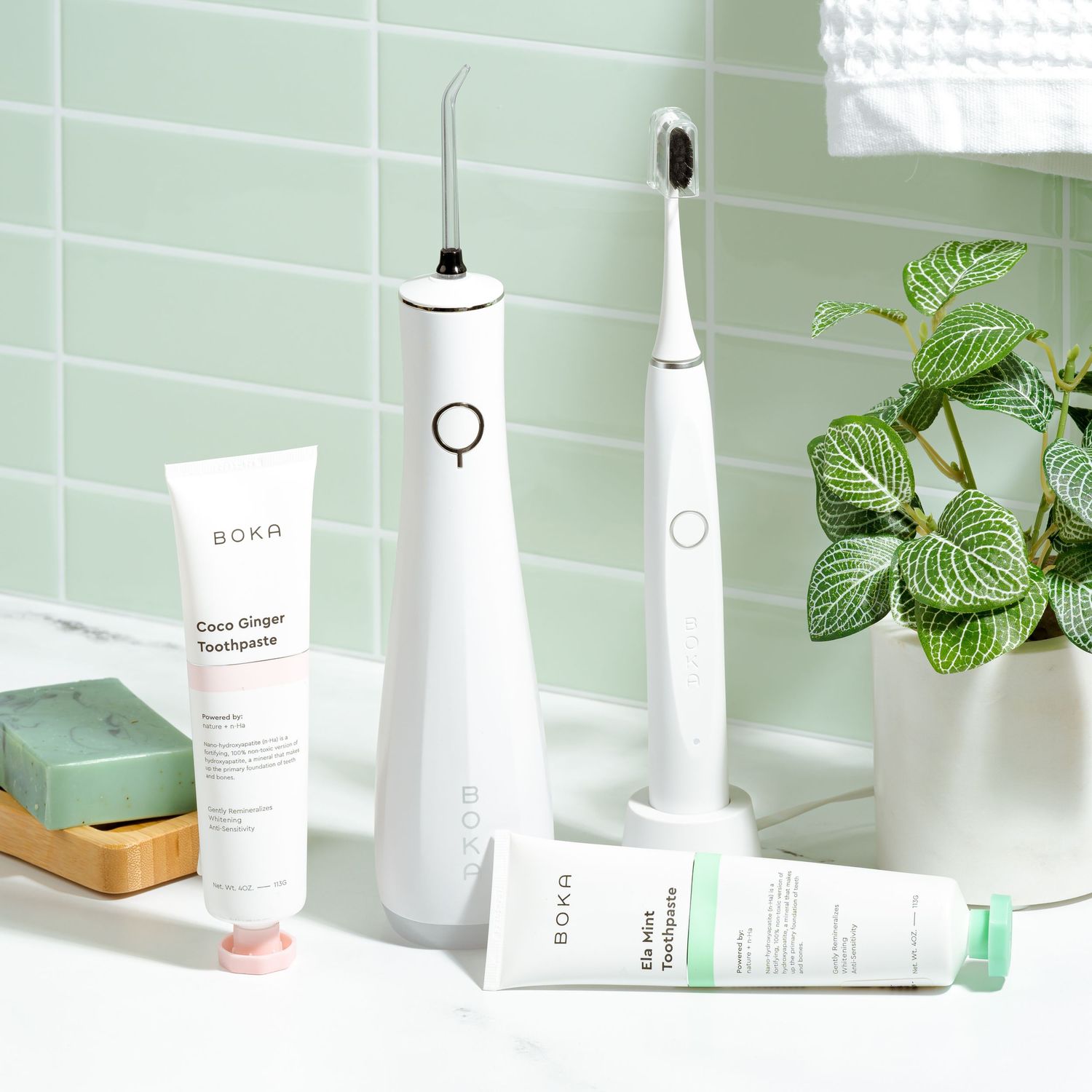 Modern electric toothbrushes and skincare products displayed with green plant on bathroom counter.