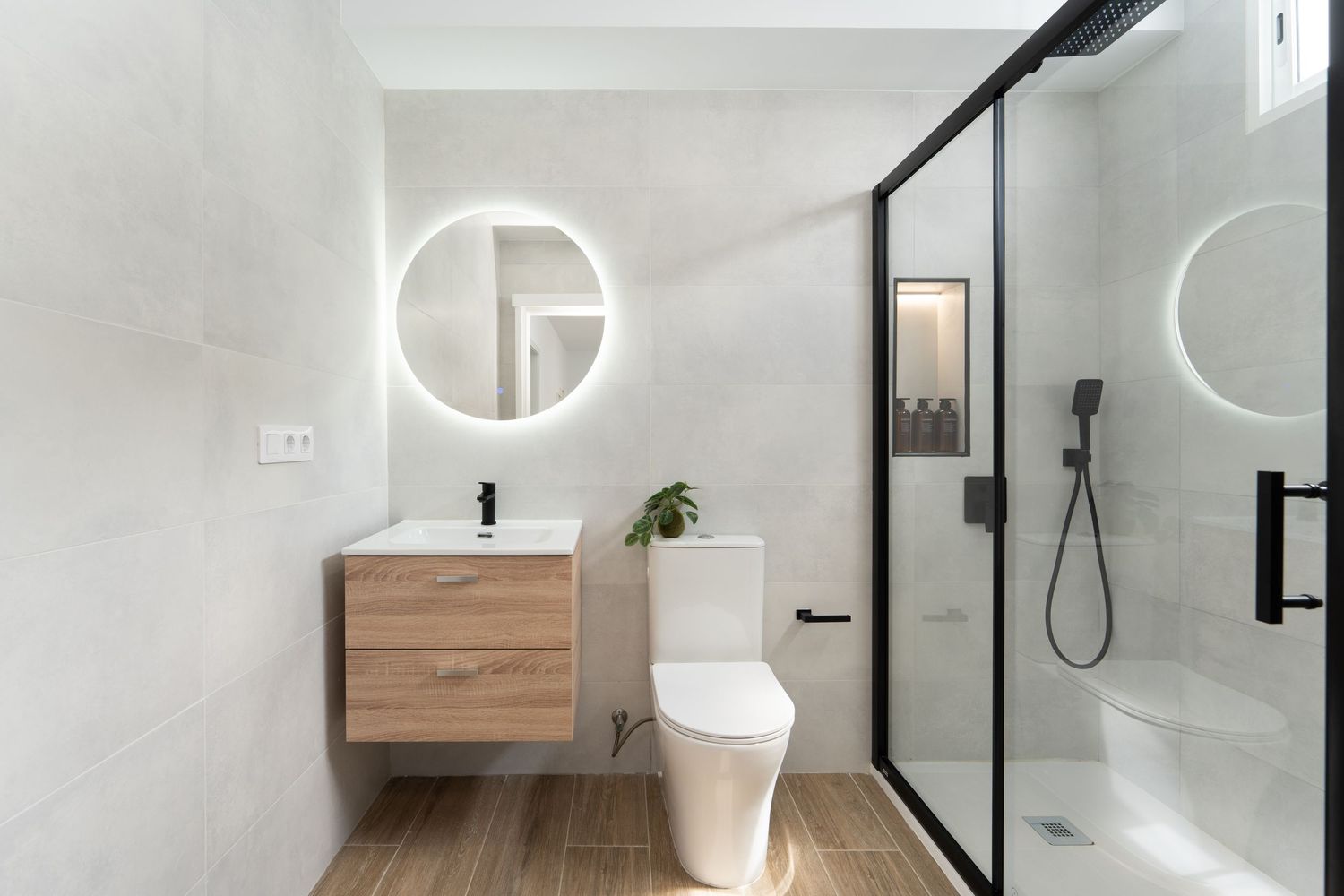 Modern minimalist bathroom featuring round LED mirrors, floating wood vanity, and glass shower enclosure with black frames.