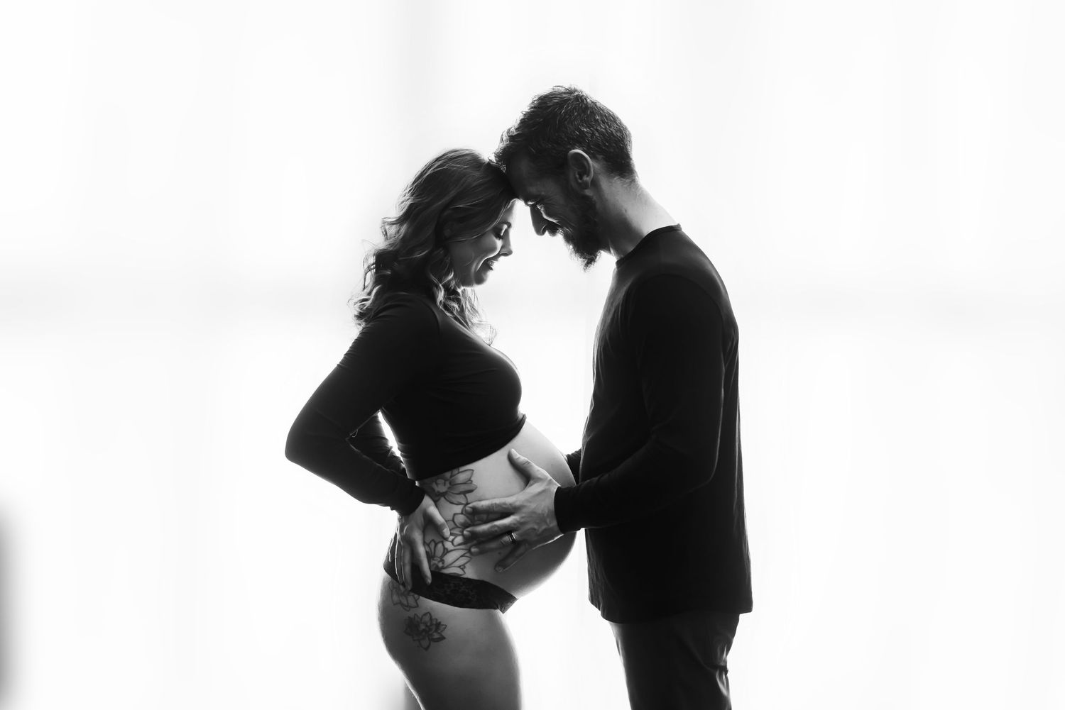 A romantic black and white maternity photo shows a couple in silhouette touching foreheads in an intimate moment.