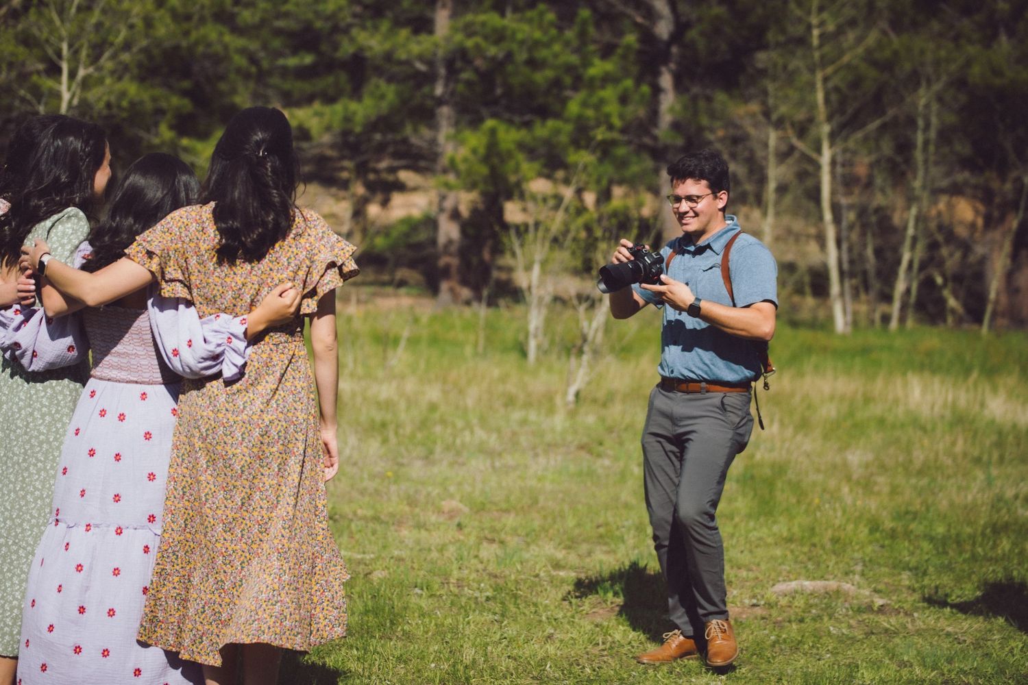A group of people in casual attire dancing and laughing in a grassy field with trees in the background.