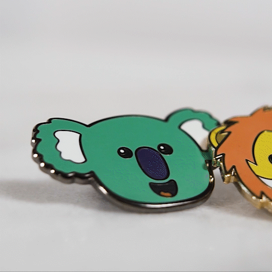 Closeup photo showing parts of small colorful cartoon animal enamel pins against a light gray background.