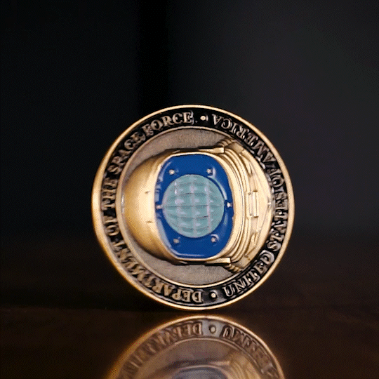 Gold and blue commemorative coin with globe design shown standing on reflective black surface.