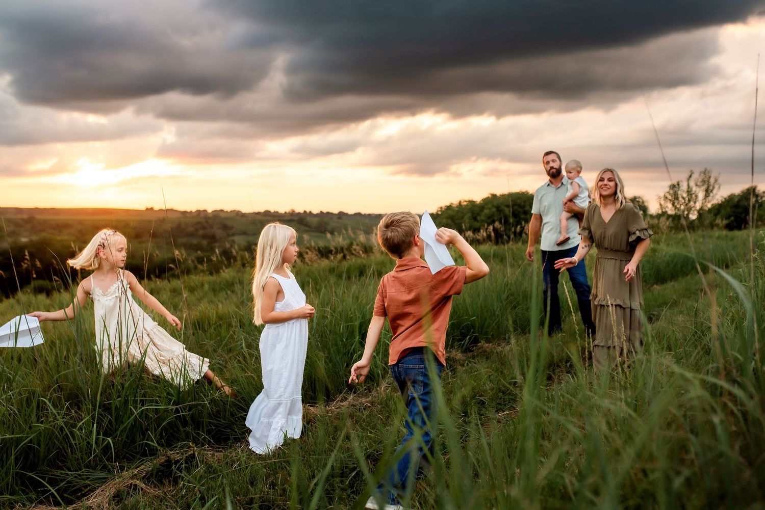 A group walks through tall grass at sunset with dramatic storm clouds overhead in a rural field.