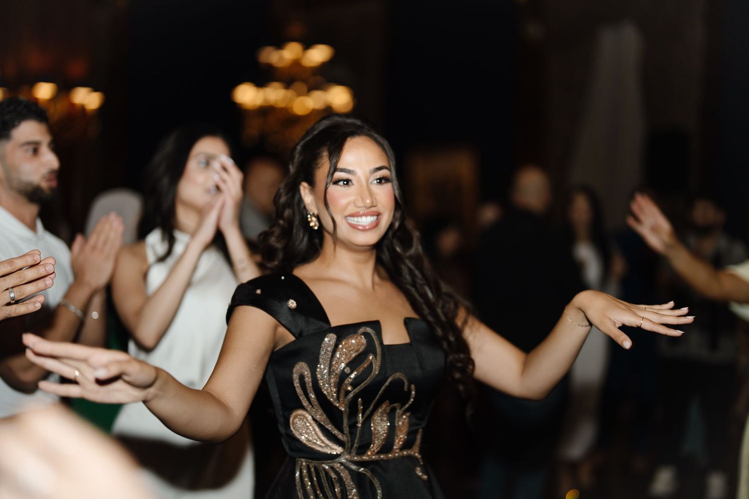 Joyful woman in black and gold embroidered dress dancing at elegant wedding reception celebration.