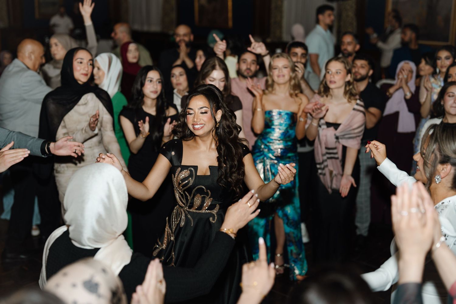 Joyful woman in black gown dancing with crowd at lively elegant wedding reception celebration.