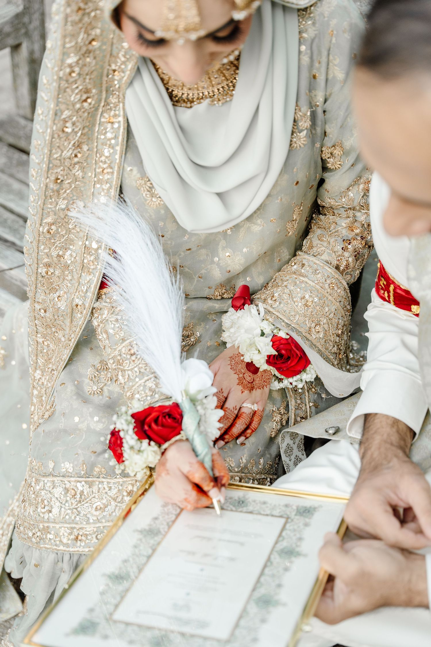 Muslim bride signing nikah marriage contract with decorative feather pen adorned with red roses and white flowers.