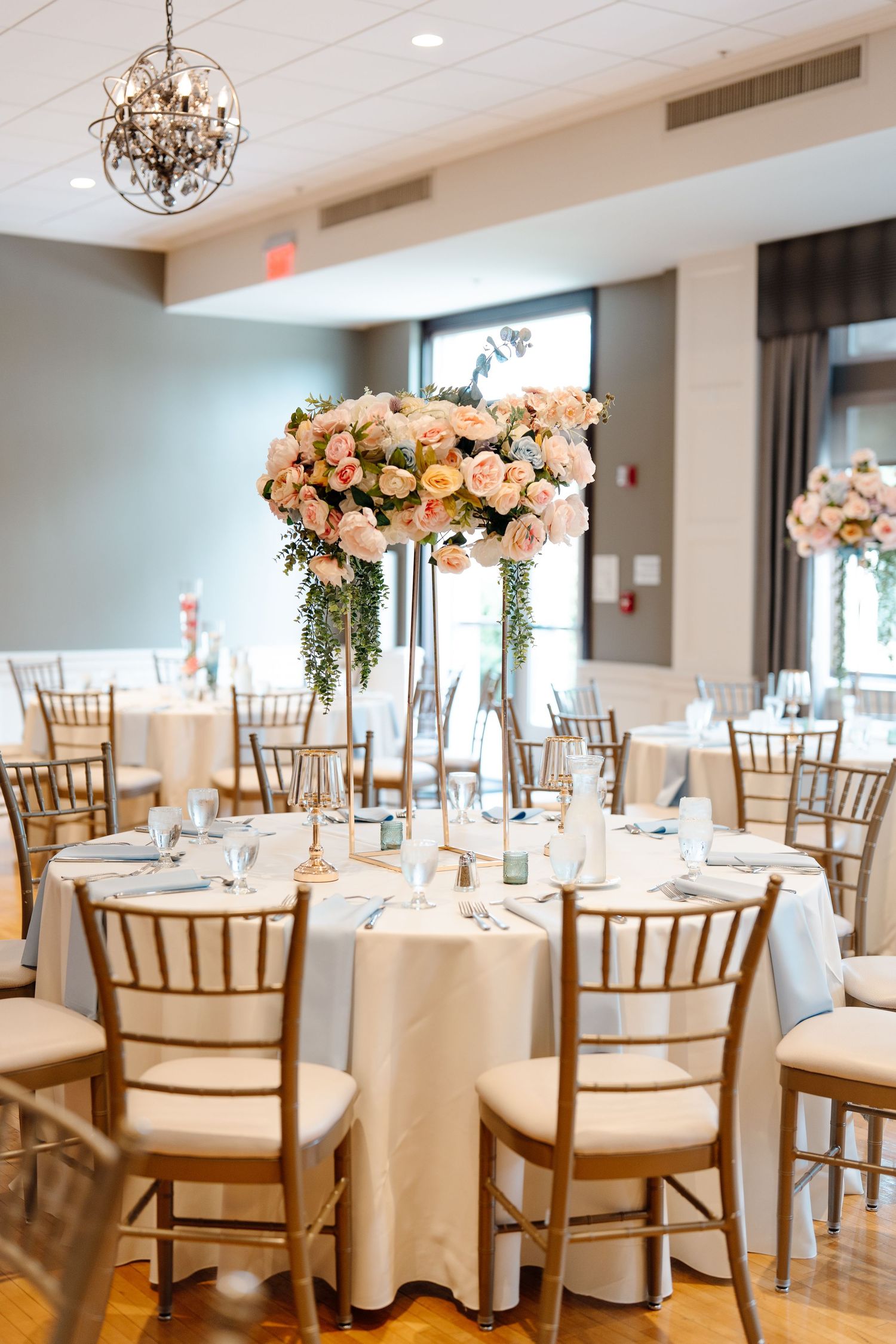 Elegant wedding reception venue with tall floral centerpieces of pink roses on white draped tables.