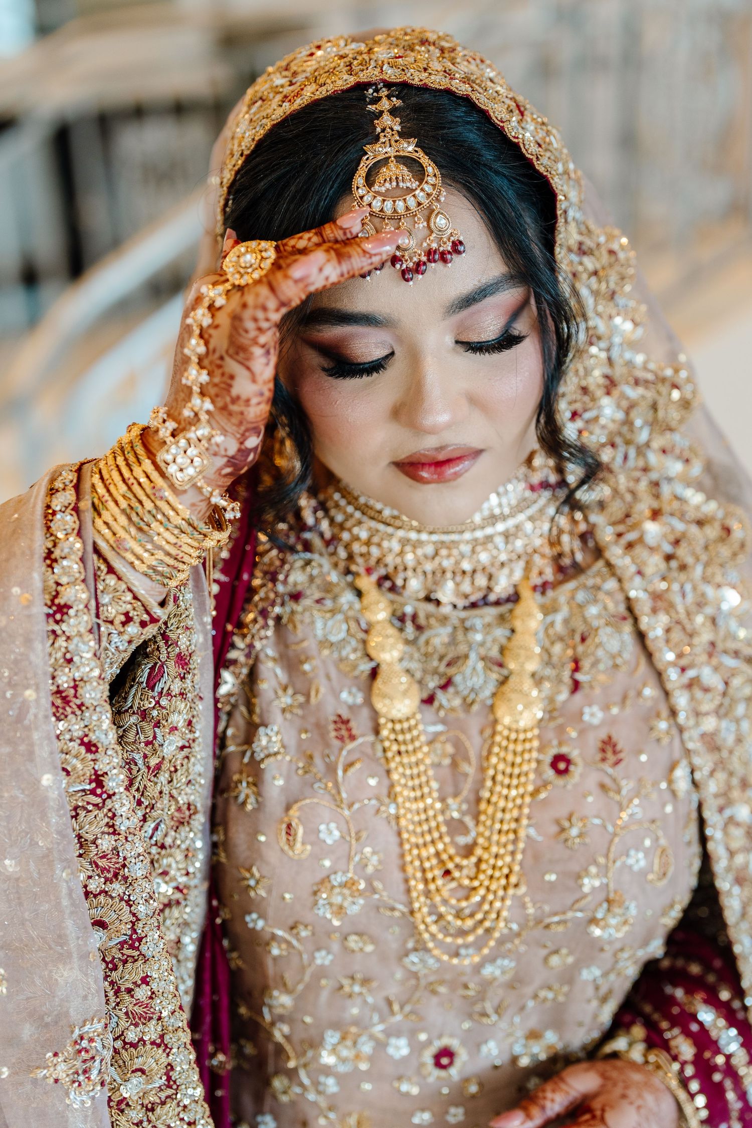 Close-up portrait of South Asian bride in gold embroidered bridal attire with elaborate gold jewelry and maang tikka.