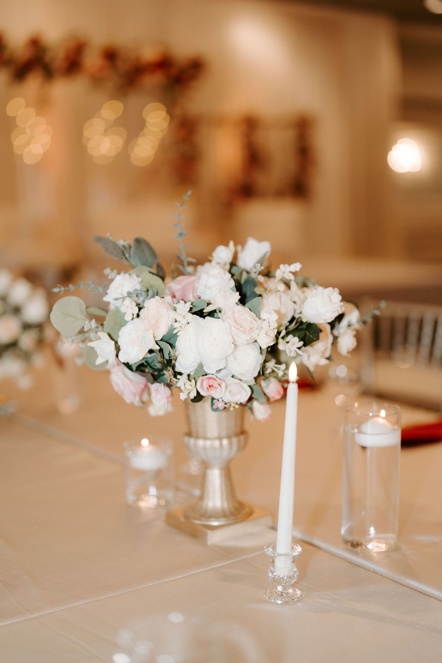 Elegant wedding table centerpiece with white and blush roses in silver urn vase with taper candles.