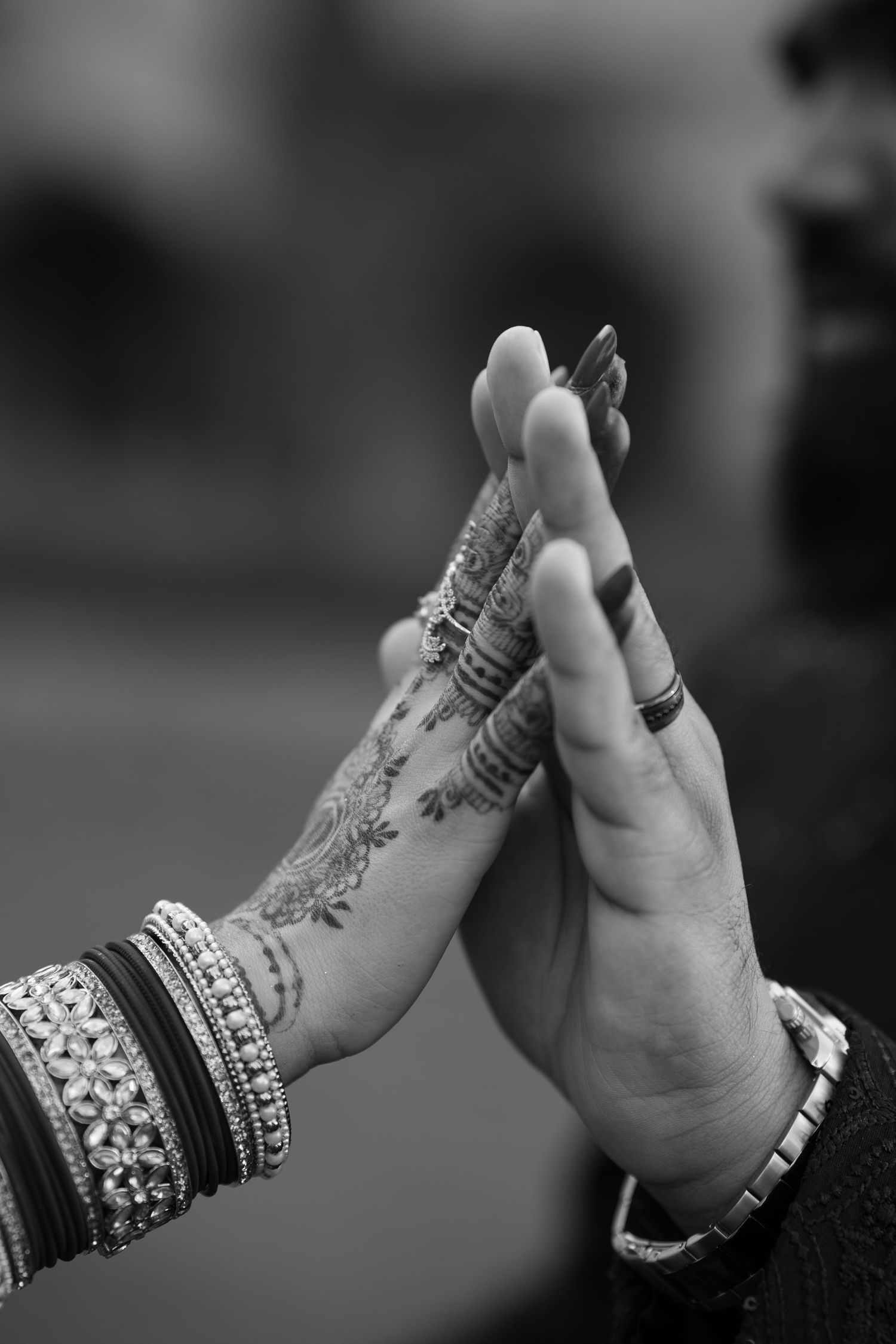 Black and white close-up of Indian bride and groom pressing hands together showing mehndi and bangles.