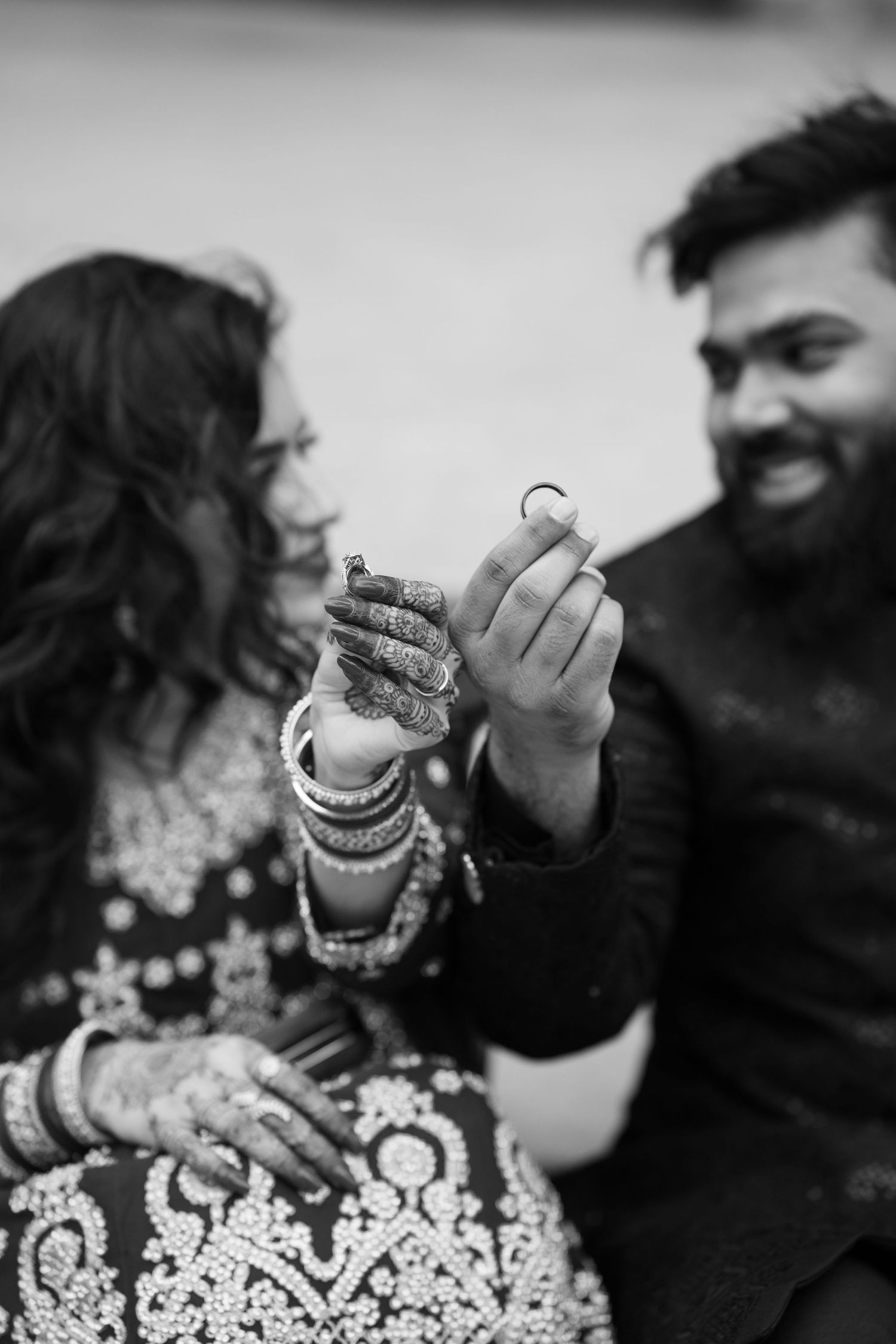 Black and white photo of South Asian couple smiling while groom holds up wedding ring.