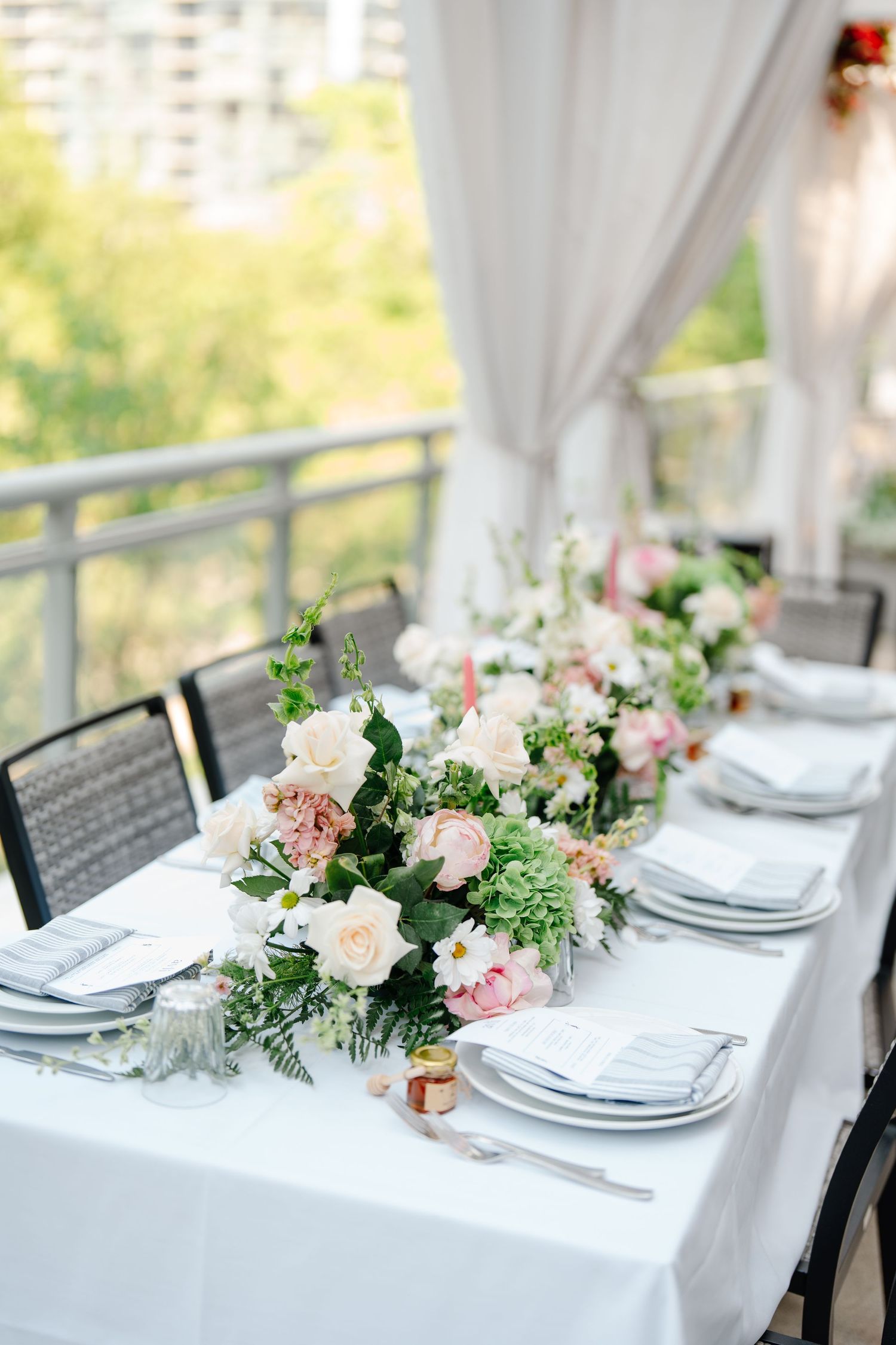 Elegant wedding table setting with blush and white floral centerpiece on white linen outdoors.