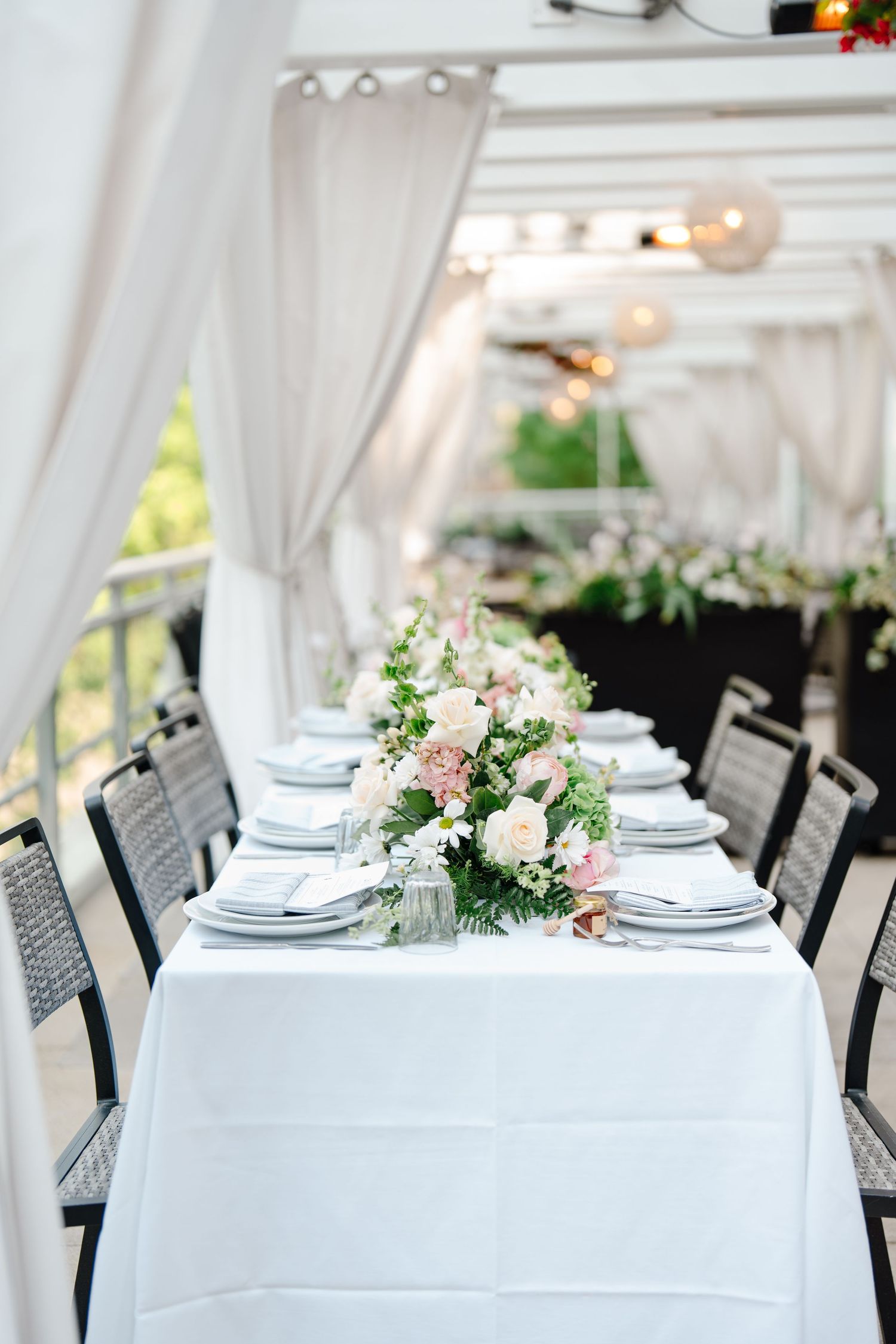 Long wedding reception table with pink and white floral runner under draped white canopy.