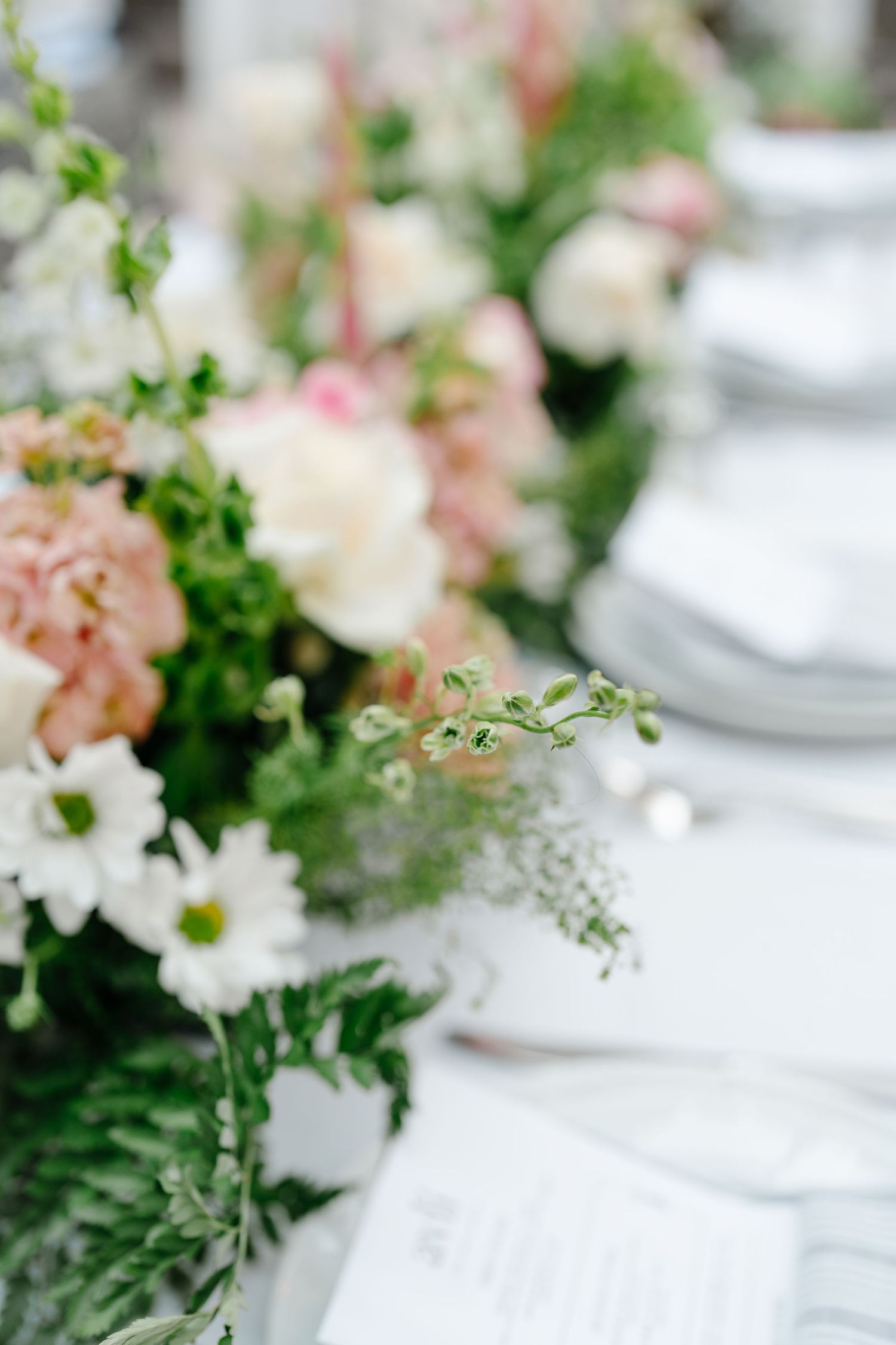 Close-up of lush wedding centerpiece with blush roses, carnations, and white daisies.