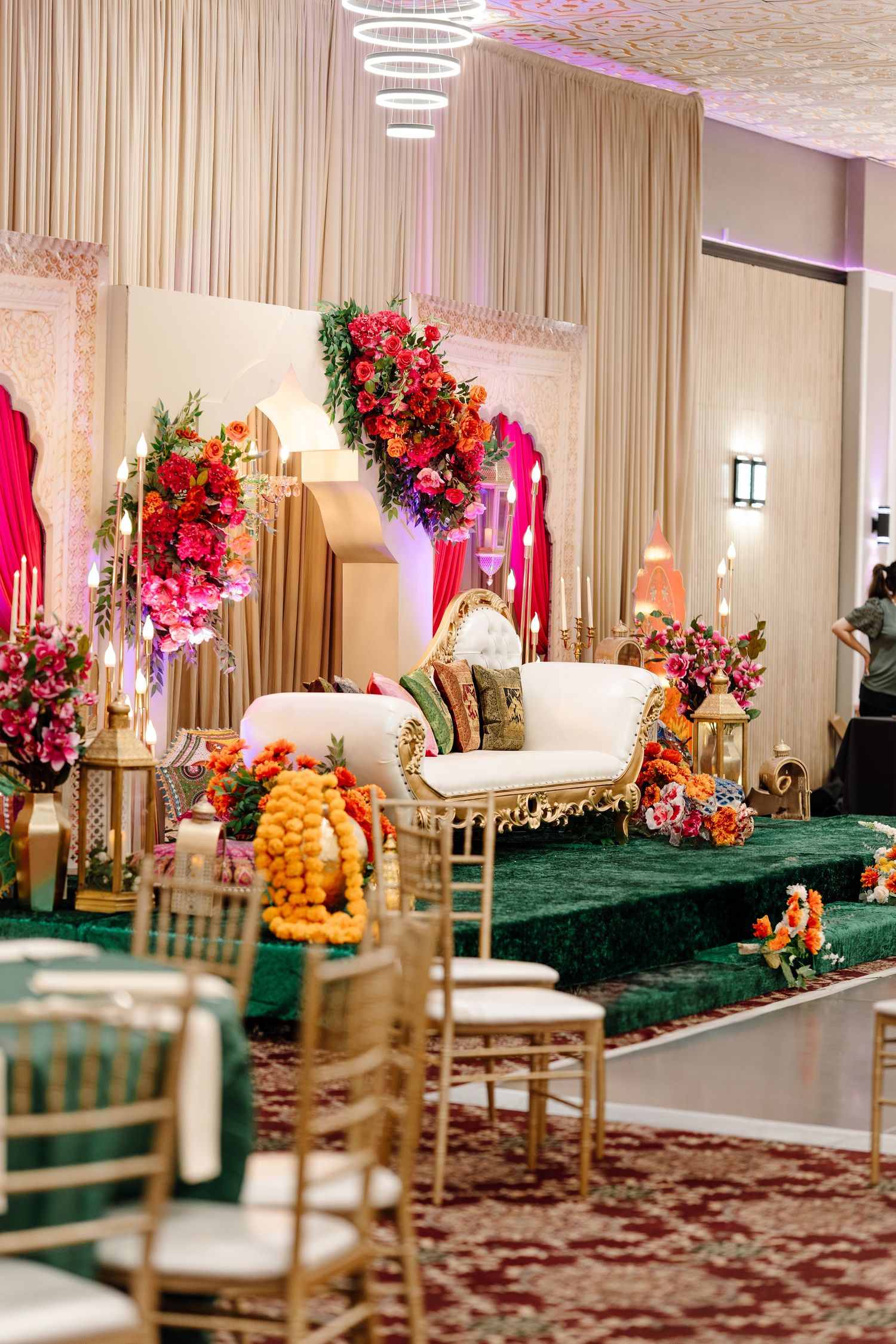 Luxurious South Asian wedding venue with white sofa, colorful floral arrangements and green velvet stage decor.