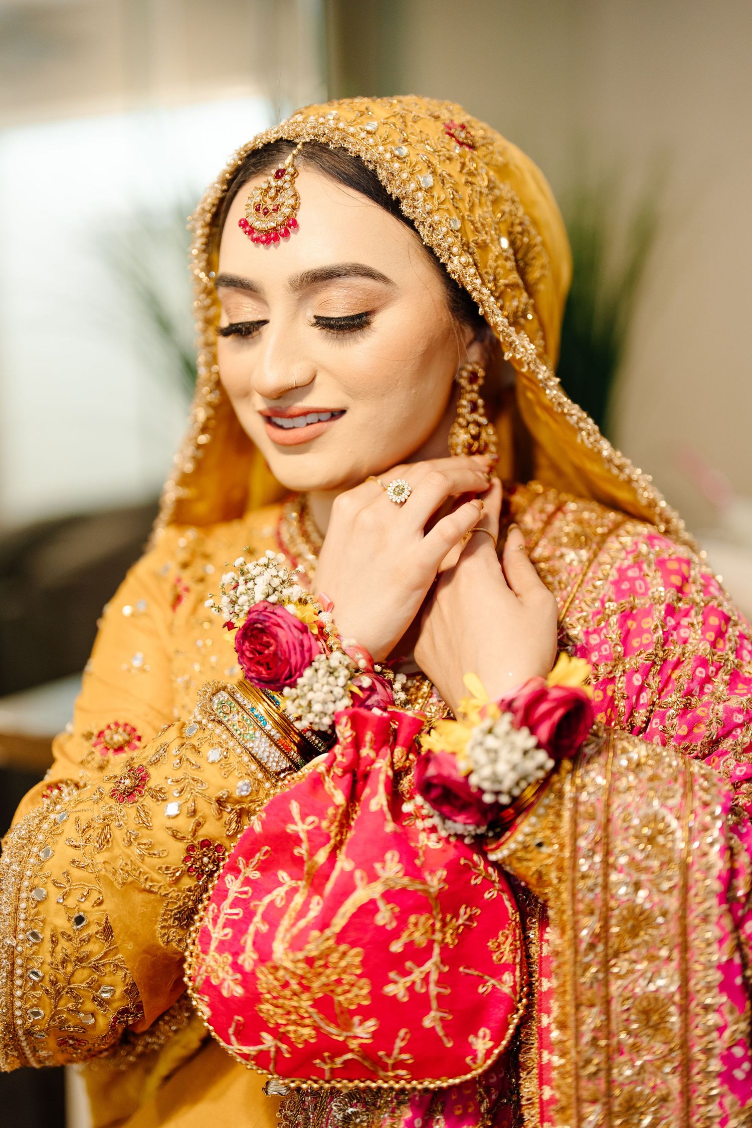 South Asian bride in golden embroidered bridal outfit holding red potli bag with floral wrist accessories.