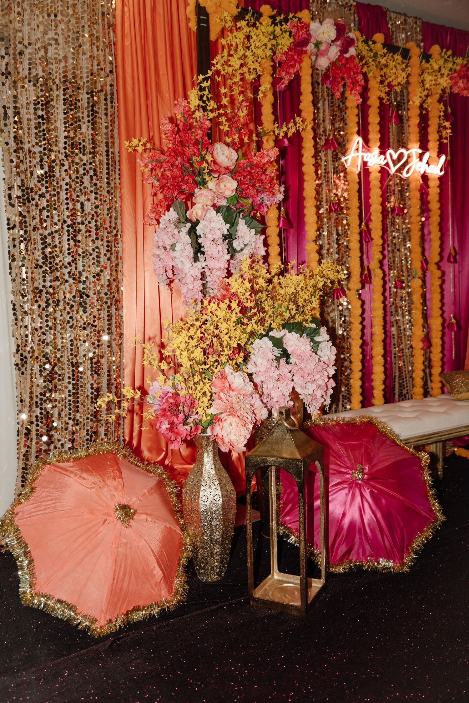 Vibrant South Asian wedding mehndi decor with colorful flowers, sequin backdrop, and decorative umbrellas.