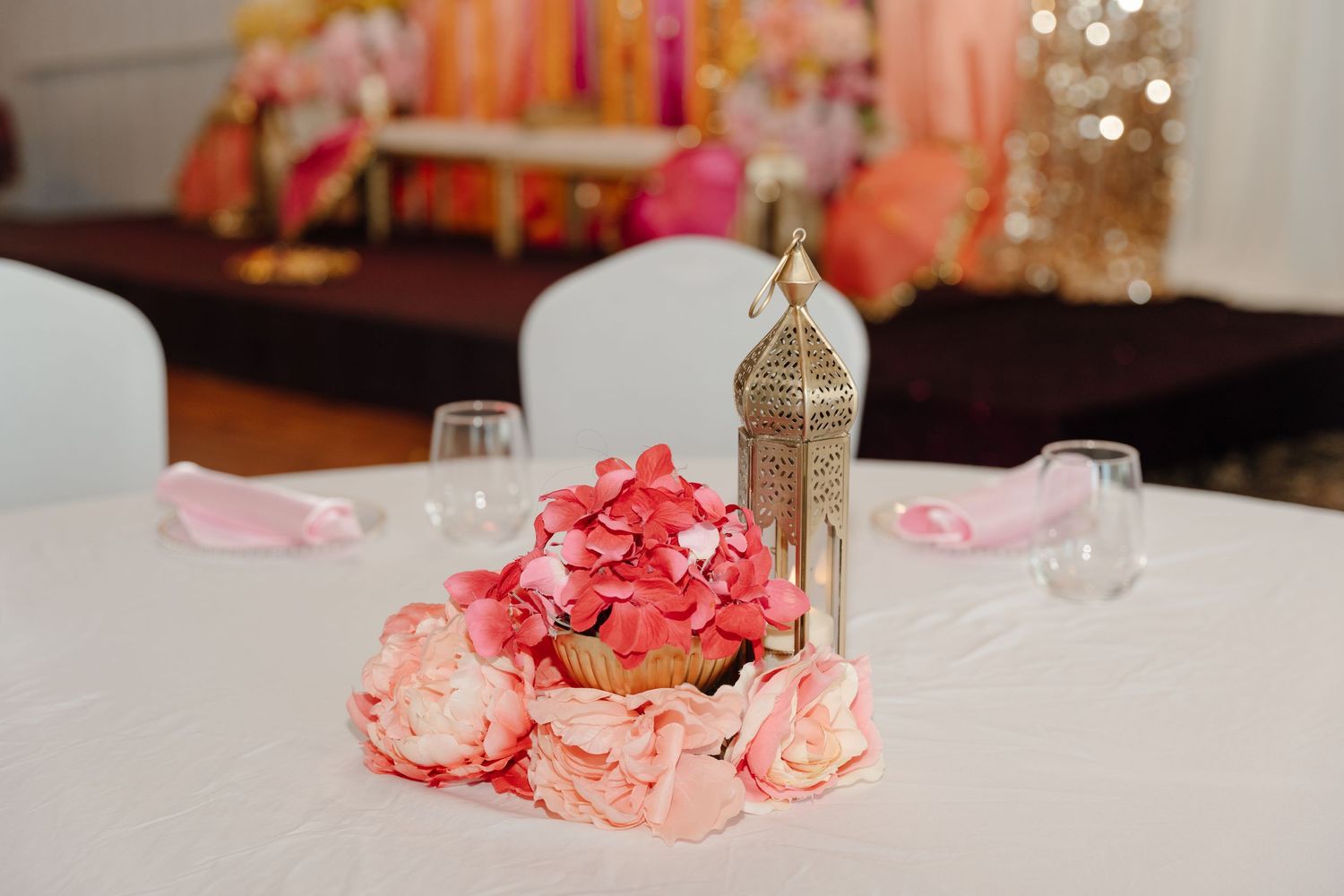 Pink hydrangea and rose centerpiece with gold Moroccan lantern on white wedding reception table.