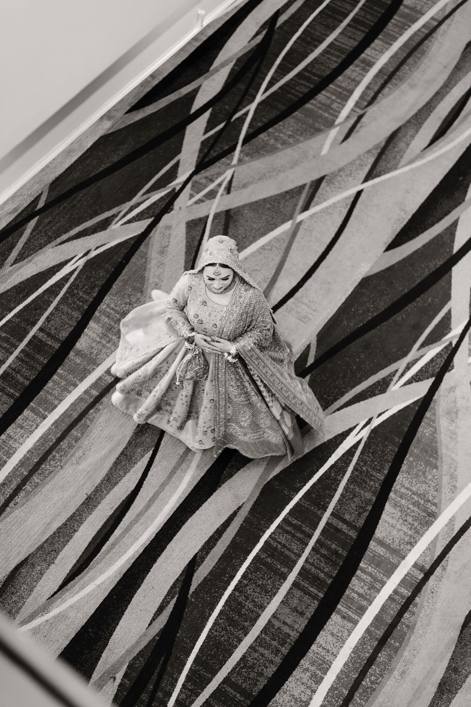 Aerial black and white artistic photo of South Asian bride in embroidered lehenga on geometric patterned floor.