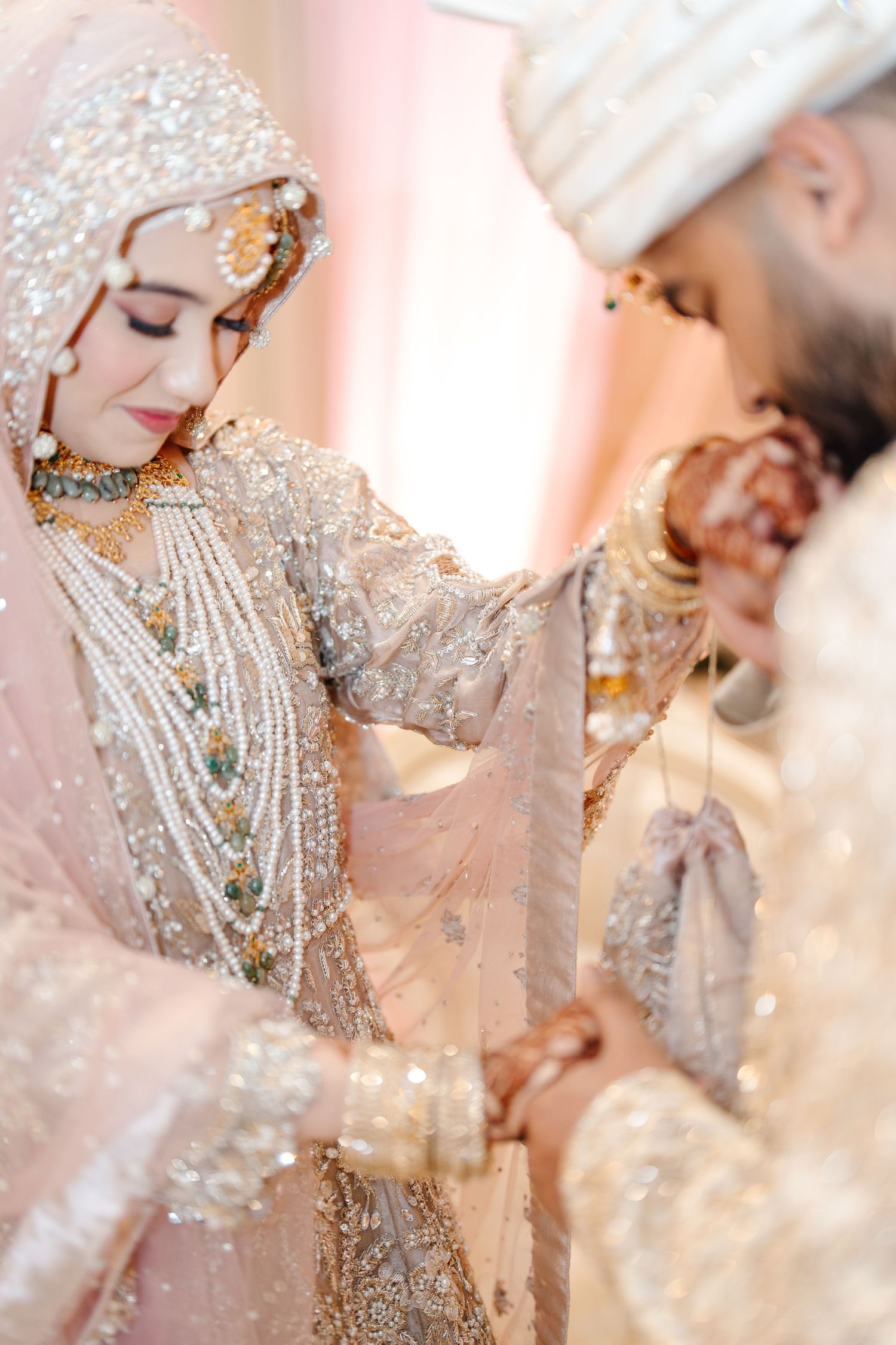 Pakistani bride in pearl-adorned ivory bridal outfit holding grooms hand during nikah ceremony.