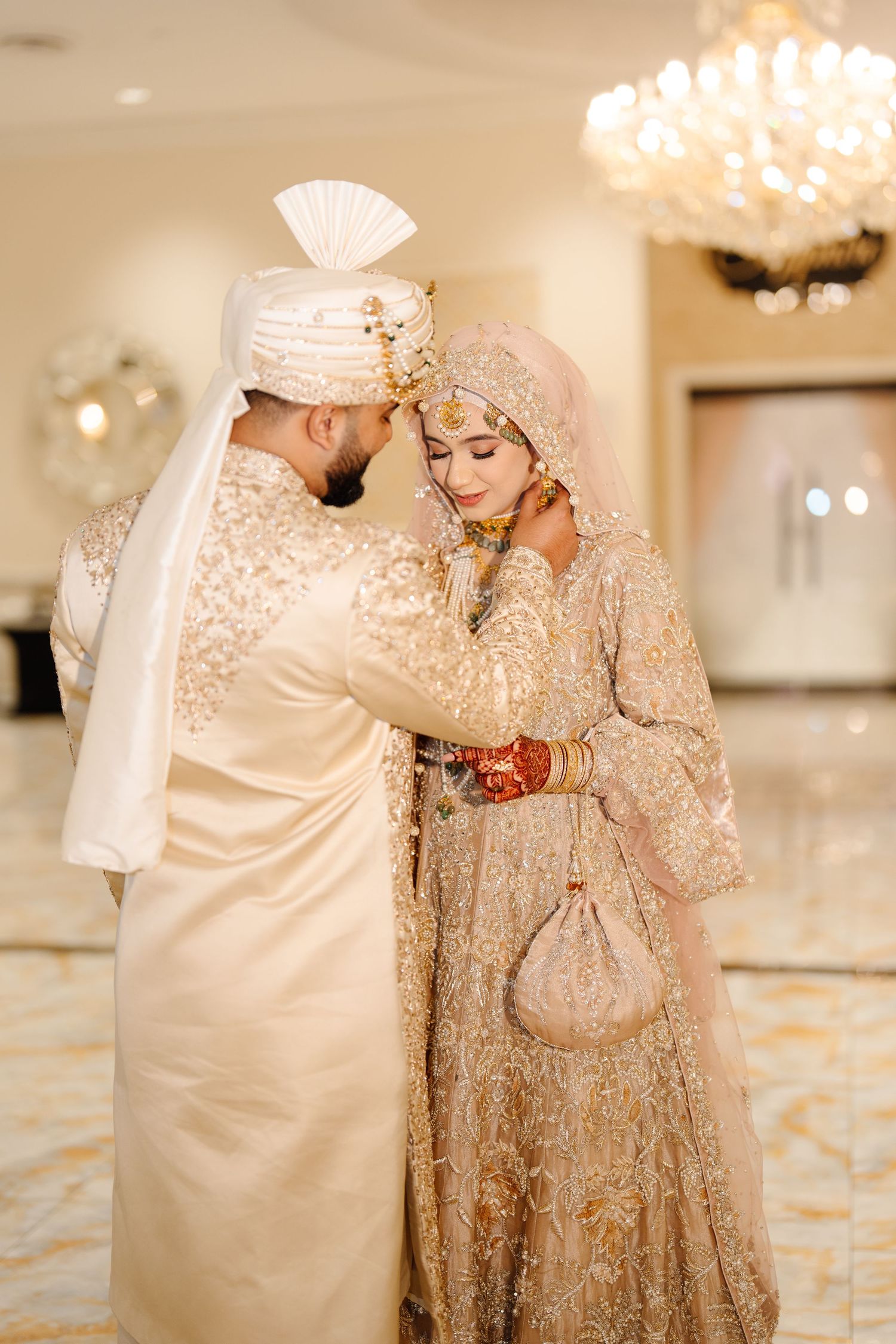 South Asian groom in cream sherwani tenderly embracing bride in gold embroidered wedding outfit.