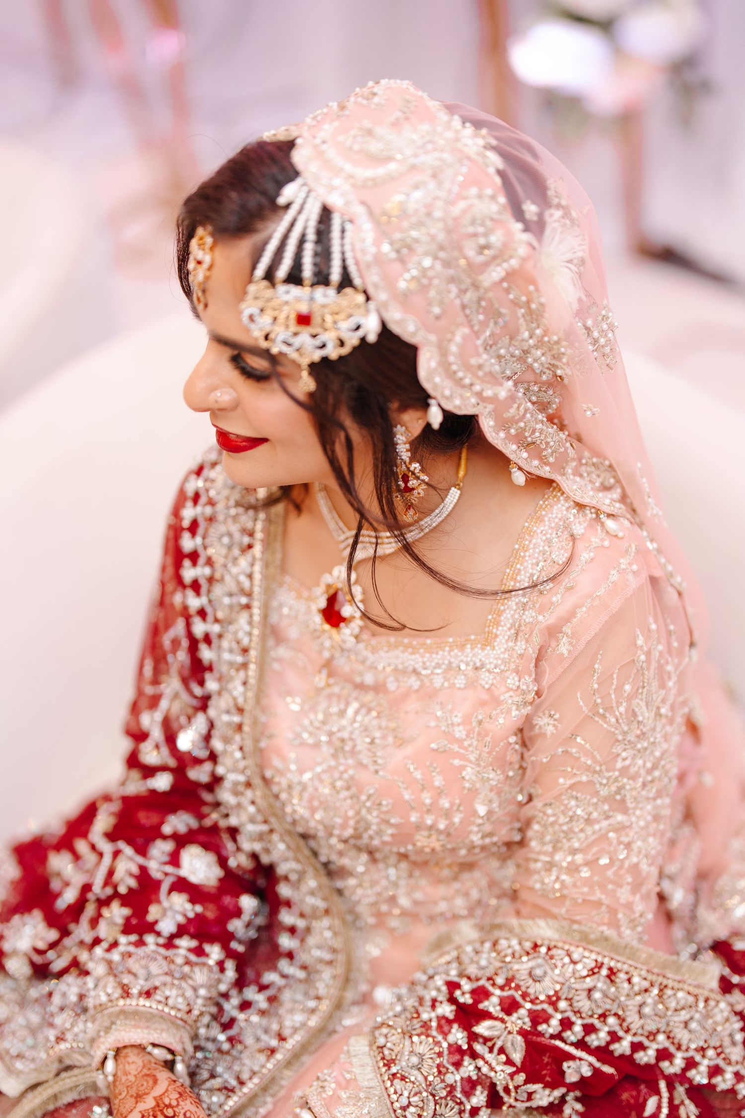 Pakistani bride in pink embroidered bridal outfit with pearl maang tikka and dupatta, elegant side profile view.