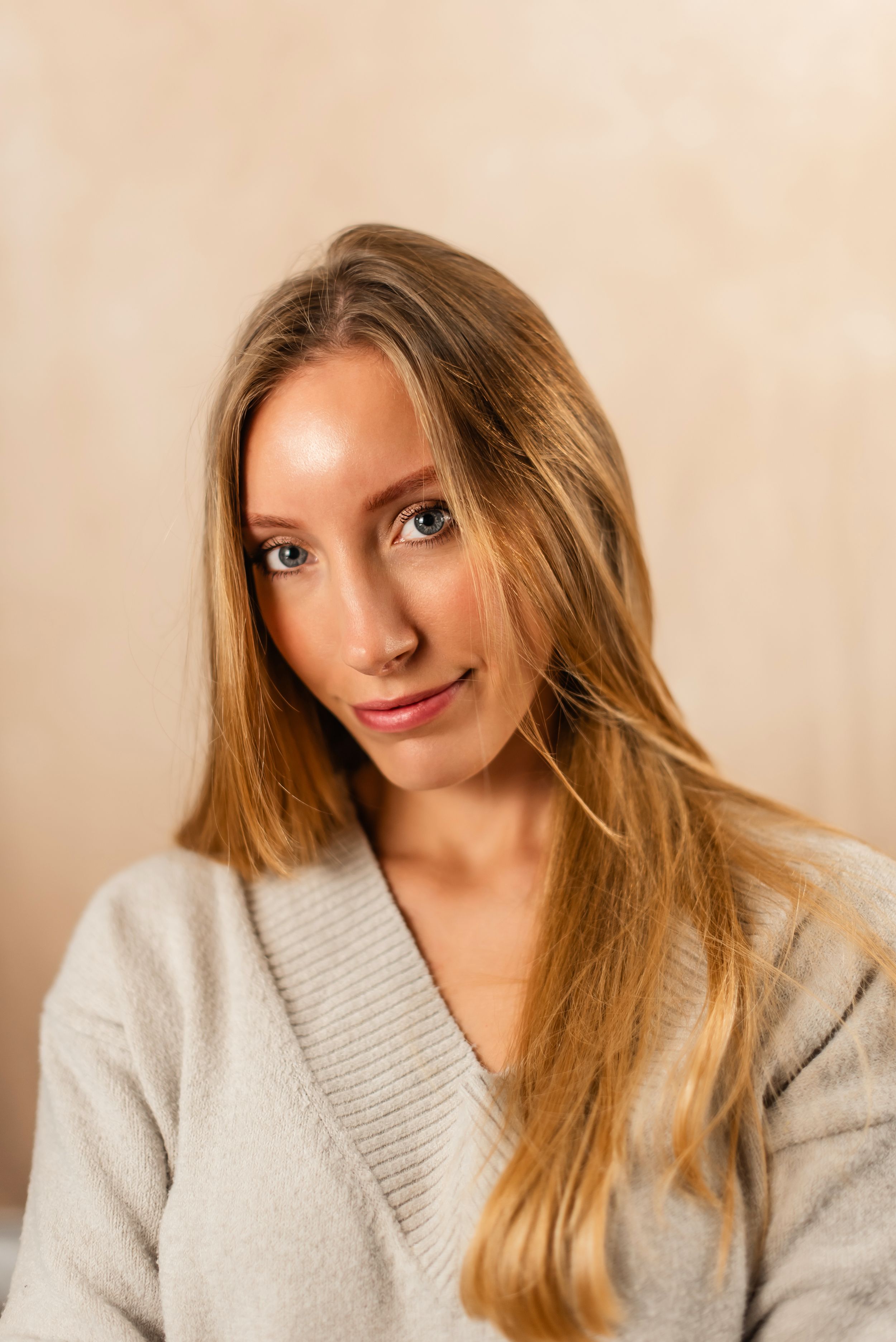 Portrait of someone with long honey blonde hair wearing a beige knit sweater against a neutral background.