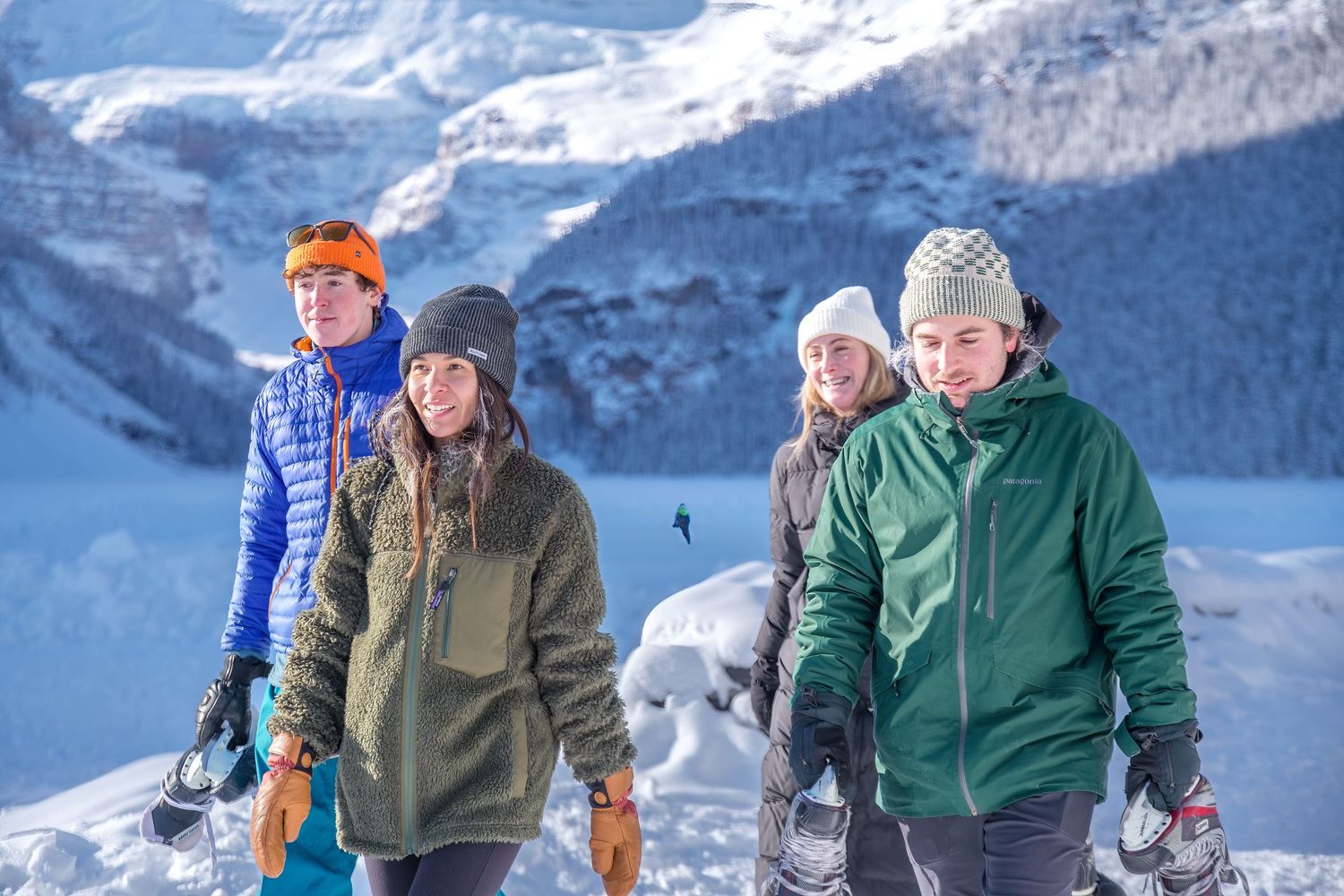 Skiers ascending a snowy mountain slope on a clear winter day with rugged peaks in the background.