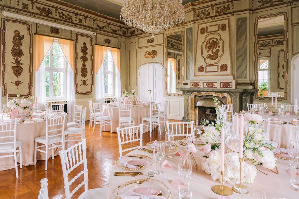 An elegant white and gold ballroom with crystal chandeliers and ornate decorations set up for a formal event.