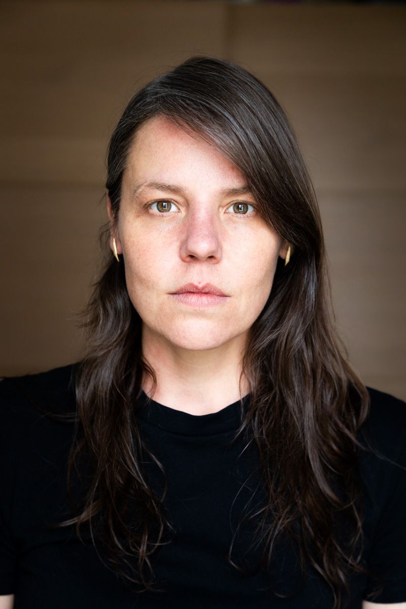 Portrait photo showing someone with long dark hair and a black shirt against a neutral background.