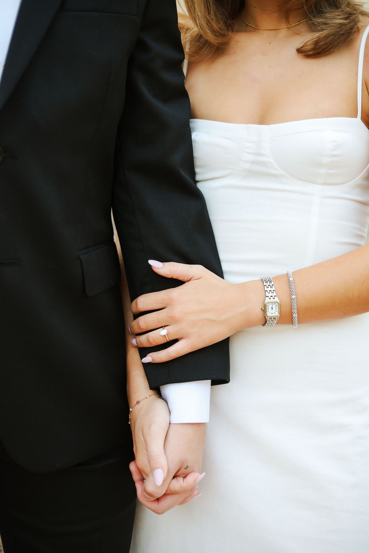 Close-up details of bride and groom's formal attire showing hands and jewelry.