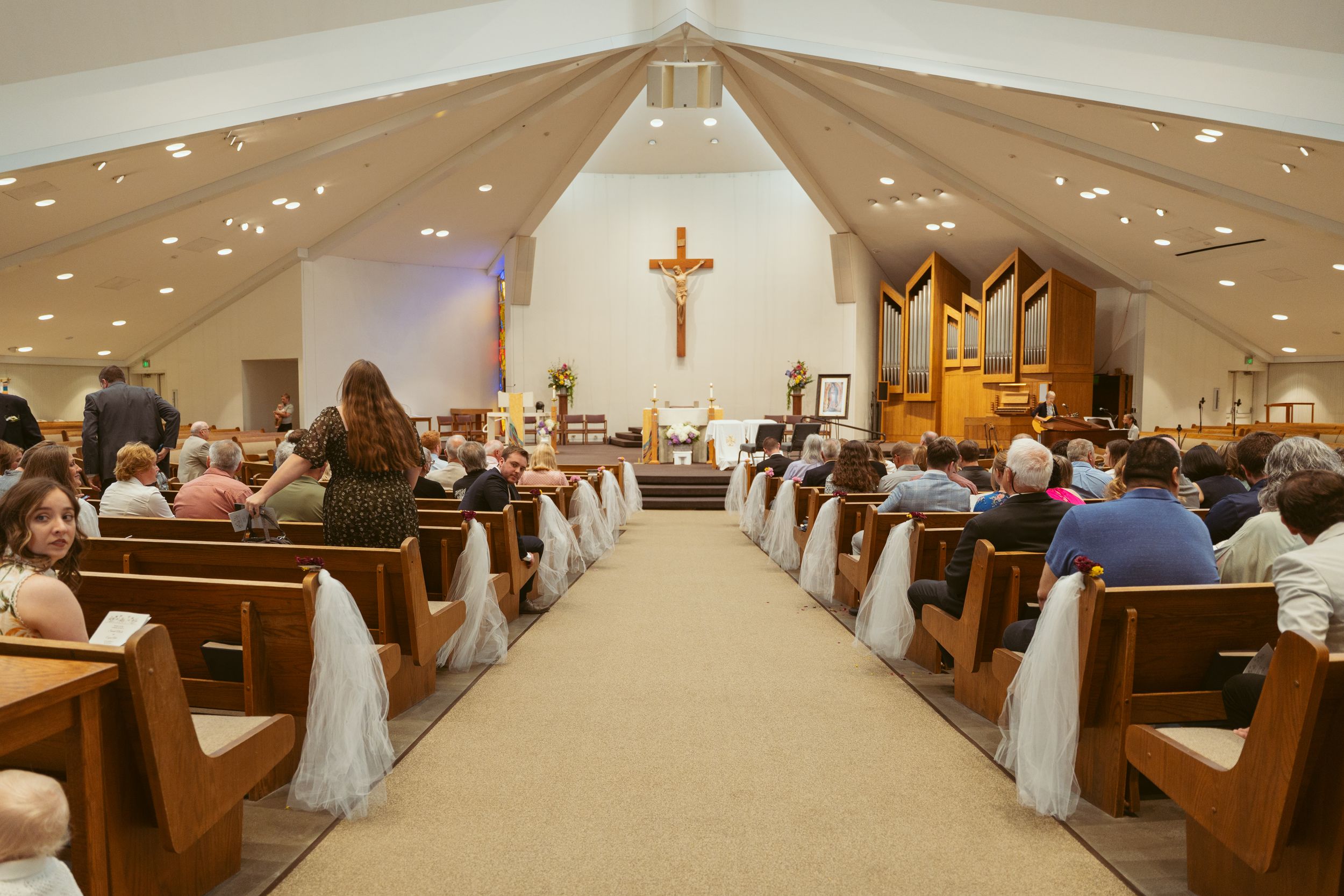 Interior view of a church sanctuary with wooden pews and a cross mounted at the front.