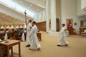 Priests in white robes prostrate themselves on the floor during an ordination ceremony.