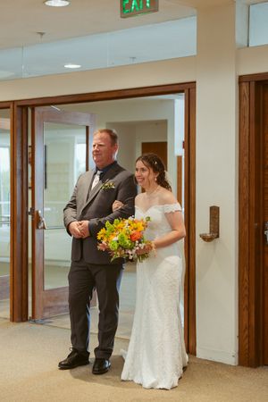 Wedding party gathers in a carpeted hallway with wooden doors and modern lighting fixtures.